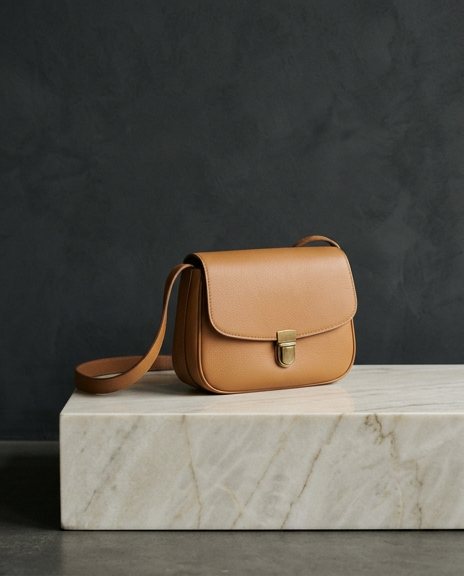 Tan leather satchel on a marble plinth against a deep charcoal wall